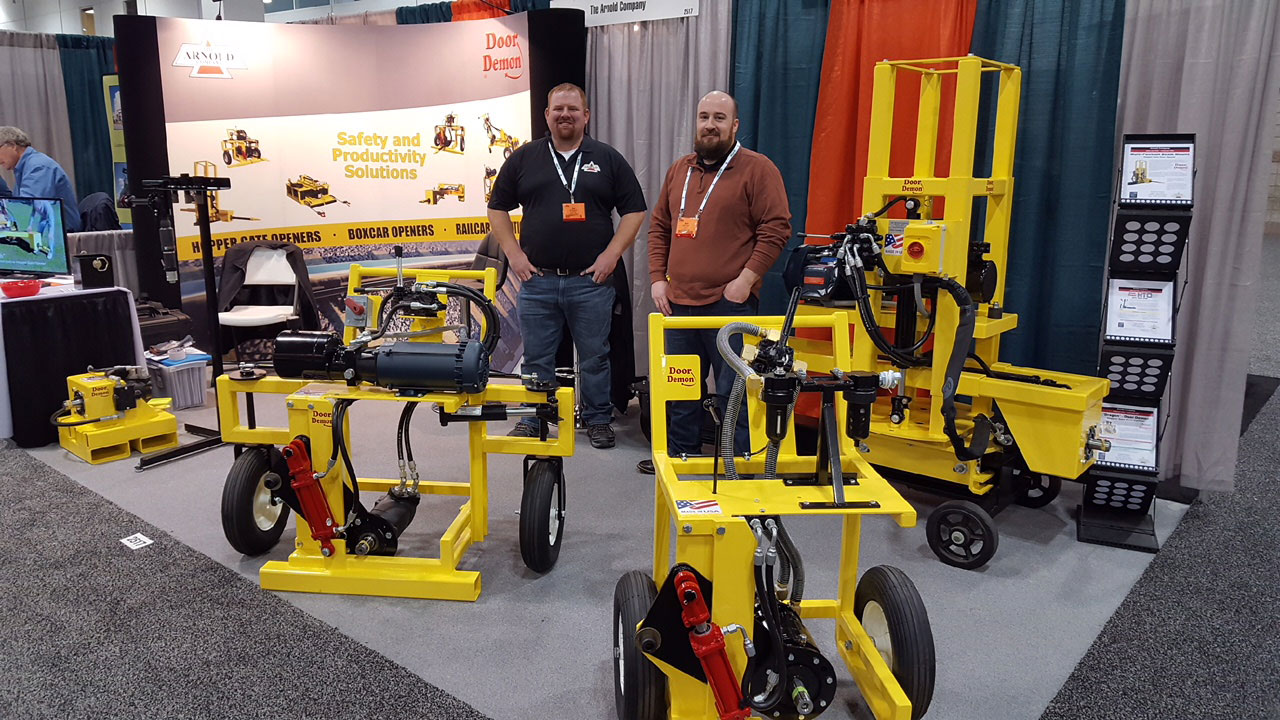 Arnold Company representatives proudly stand next to a collection of their railcar and trailer hopper gate openers.